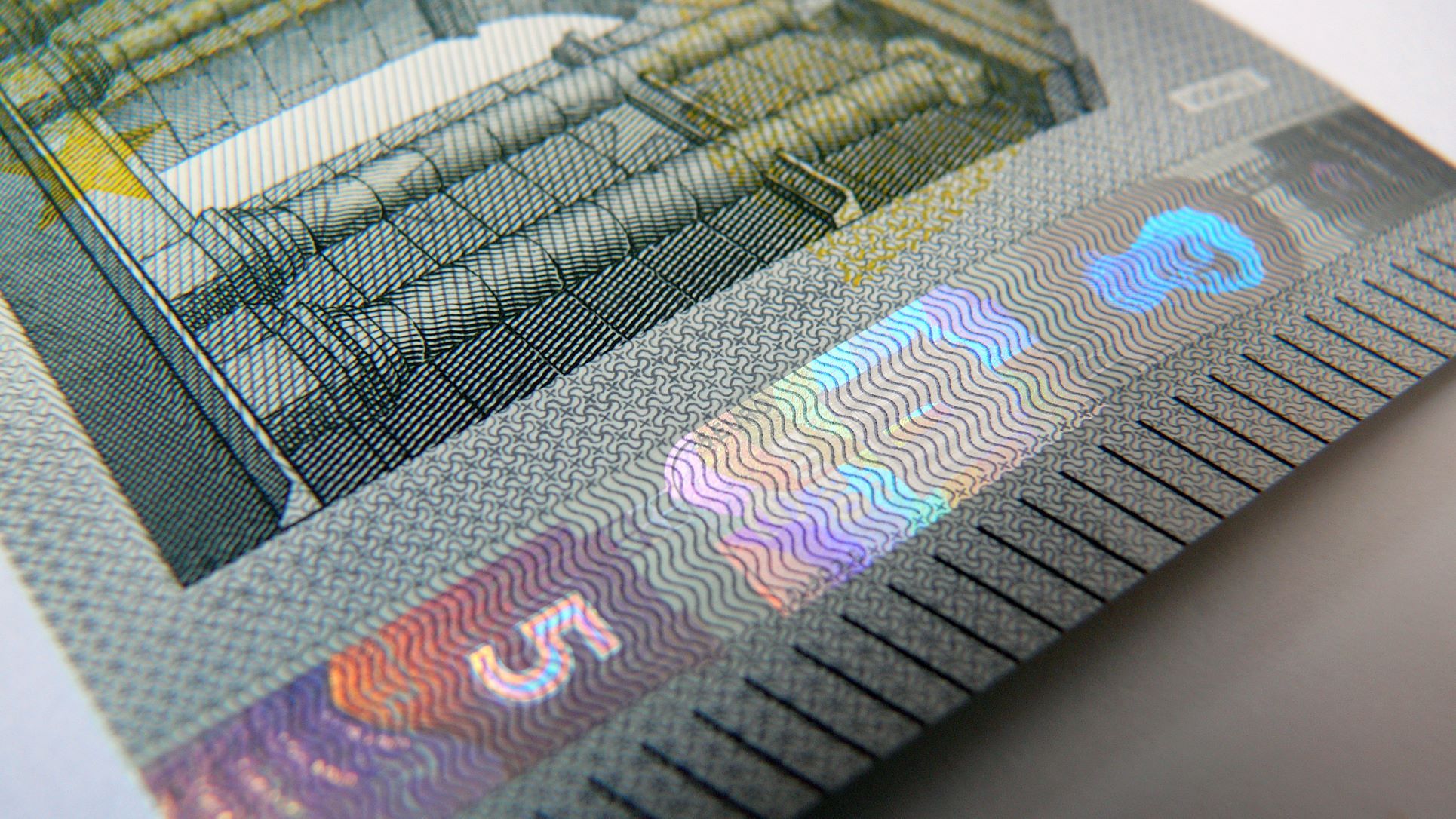 Das Bild zeigt eine Nahaufnahme eines 5-Euro-Scheins mit holografischen Sicherheitsmerkmalen, die je nach Blickwinkel ihre Farbe verändern.