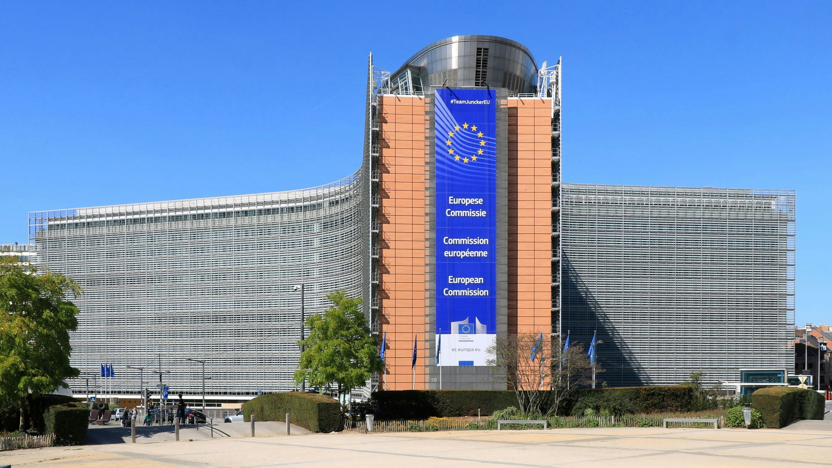 Le bâtiment Berlaymont à Bruxelles, siège de la Commission européenne, avec une grande bannière de l'UE en façade et un ciel bleu en arrière-plan.
