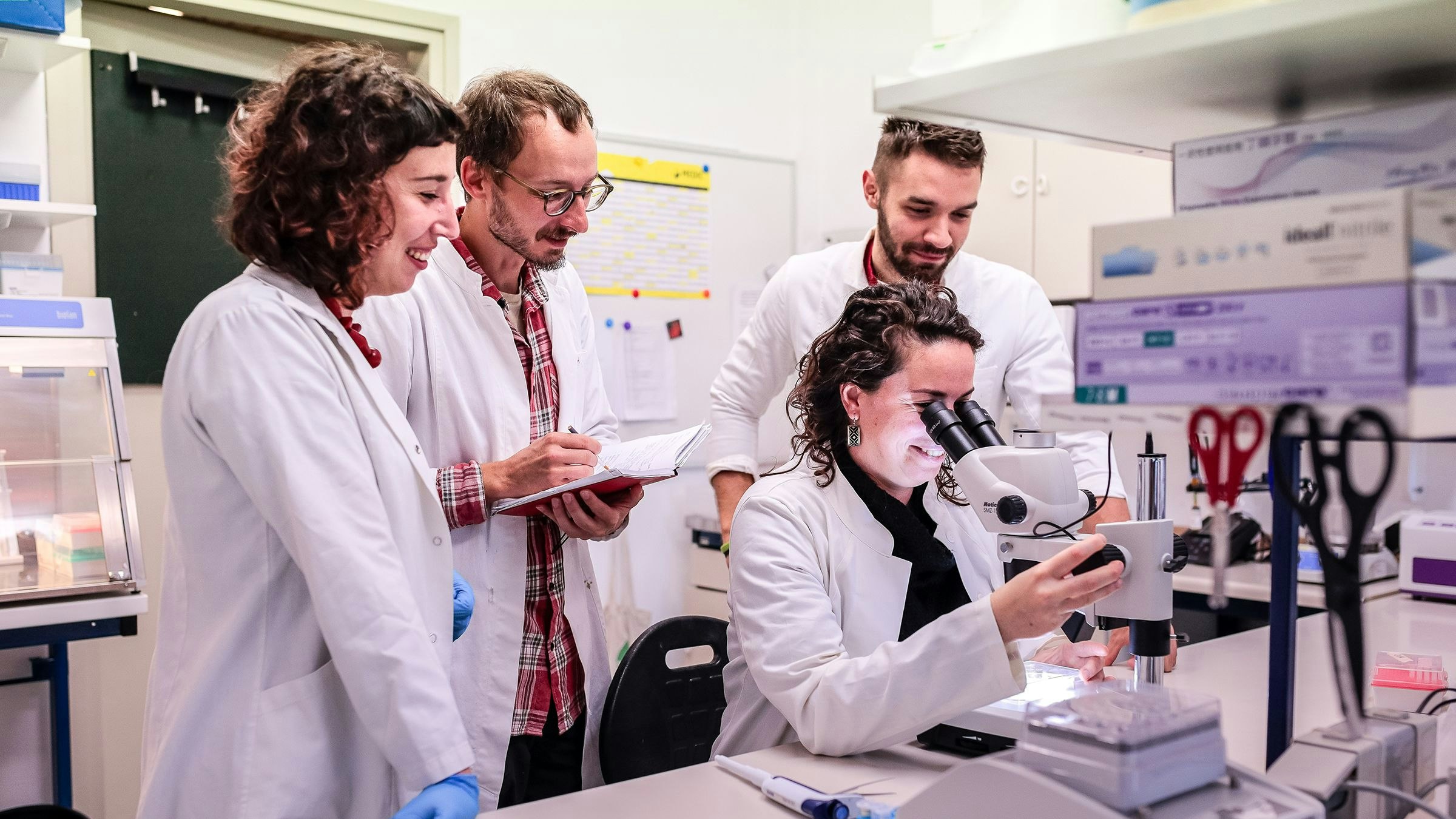 Alcuni ricercatori sono in piedi attorno a un microscopio.