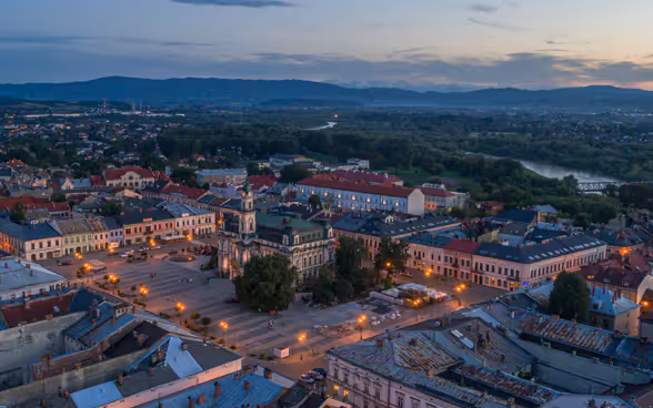 L'immagine mostra una città polacca di piccole-medie dimensioni, la sua piazza del mercato e il fiume circostante dal punto di vista di un uccello.